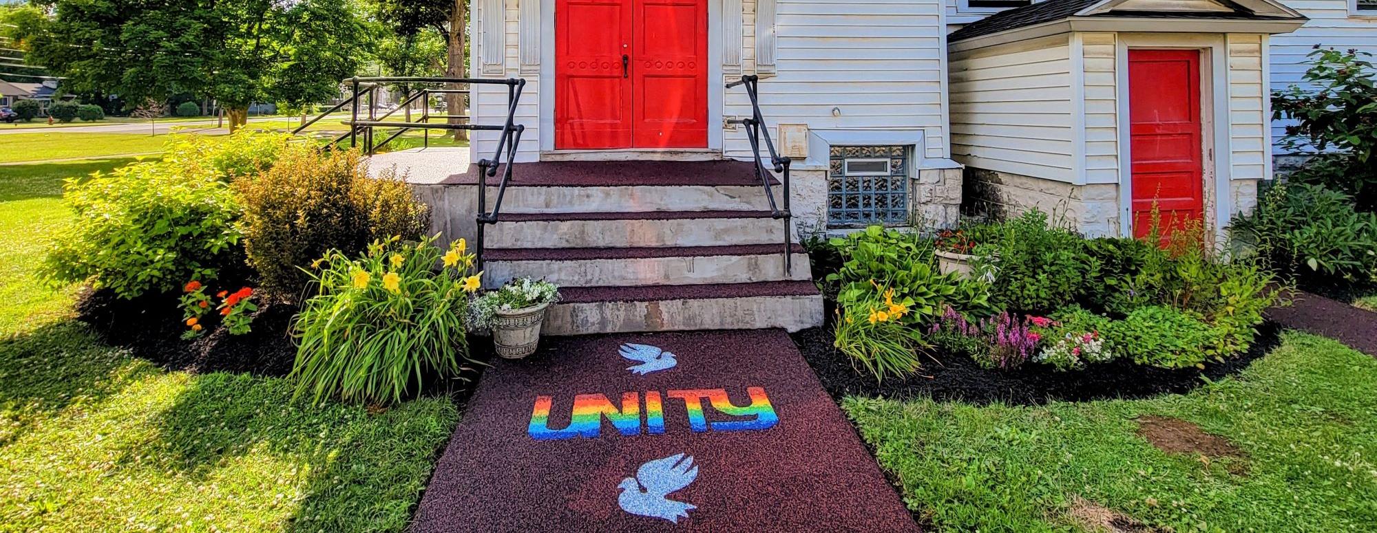 photo of main entry of the church building: red doors, rainbow UNITY logo and peace dove inlays