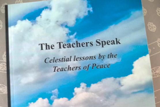 gray backdrop with a book, cover photo of blue sky and clouds and green grassy field, title 'the teachers of peace'